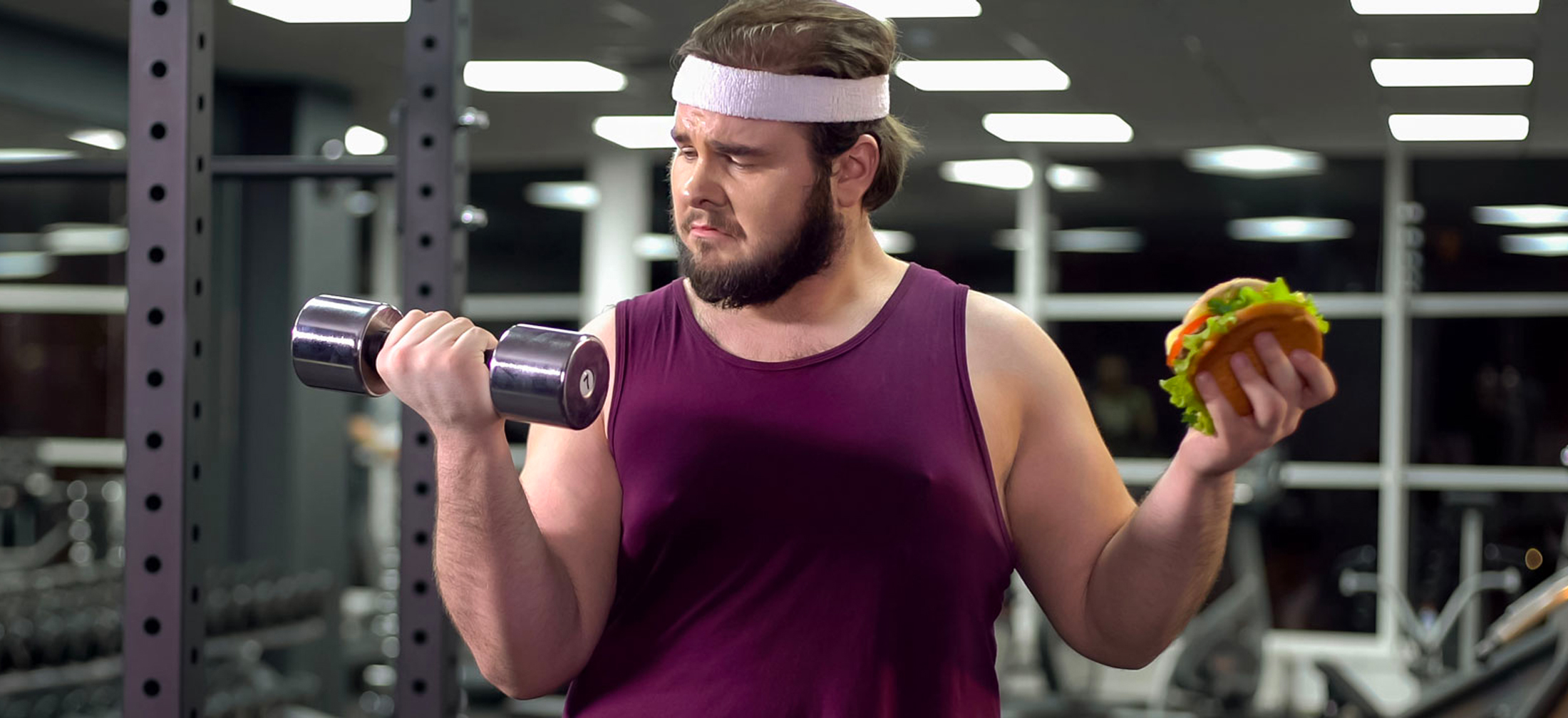 guy in gym holding weight and hamburger